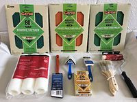 Full view of all items in the lot including sandpaper packs, paint rollers, brushes, sponge and tools on a white surface