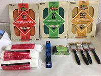 Photo showing the 3 paint roller refills, 3 sandpapers packs (120, 80, 220 grit), 4 small paint brushes, and 1 sanding block in original packaging.
