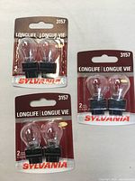Front view of three unopened Sylvania 3157 long life bulb packs showing clear glass bulbs and red packaging with branding details.