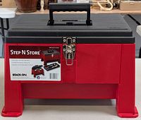 Front view of the Step N Store Step Stool Storage Box showing the red plastic base, black top lid with handle, and lockable steel draw bolt latch.