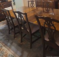 Angle showing the dining table with chairs pushed in, highlighting the carved backs of the chairs and vintage wood finish of the table surface.