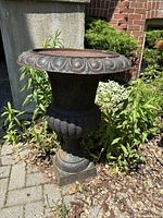 Full side view of a large cast iron garden urn showing its classical shape and rusty surface.