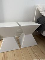 View of two white hourglass shaped side tables side by side showing their glossy surfaces and modern contour.