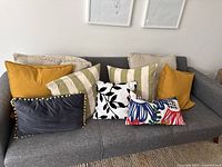 Seven decorative pillows arranged on a grey couch showing assortment and color variety.