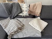 Full lot of six various decorative throws displayed on and in front of a gray sofa, showing colors and fringe details