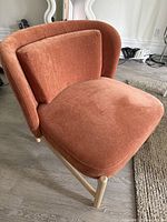 Front angle of the rust-orange fabric side chair showing the cushioned backrest and seat and light wood frame.