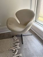 Light-colored fabric swivel chair placed near a window with natural light showing its curved ergonomic shape and metal four-prong base.