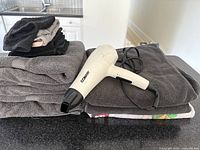Conair hair dryer placed on top of folded dark gray towels with additional assorted towels in the background.