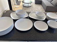 Full view of stacked IKEA white ceramic dinnerware set including plates, bowls, and platters arranged on a counter.