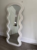 Full shot of the mirror leaning against a wall showing its wavy frame shape and overall condition