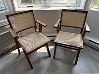 Pair of wooden armchairs with cane seats and backs, placed by window