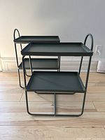 Pair of IKEA Hattasen grey metal side tables stacked together, showing full design, including two trays and tubular frame handles.