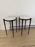 Pair of side tables with white marble tops and black metal legs.