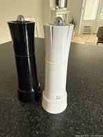 Front view of both Peugeot salt and pepper mills, black and white, standing upright on a black surface.