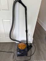 Full view of the Samsung vacuum cleaner showing hose, floor attachment, and power cord lying on the floor against a wall.