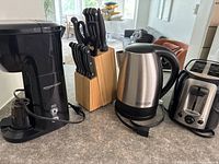 Full view of kitchen small appliances including Amazon Basics coffee maker, Hamilton Beach electric kettle, Oster toaster, and wooden block with knives.