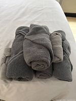 Five rolled grey towels stacked on a white surface, showing various shades of grey and terry cloth texture.