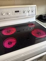 Frigidaire white electric stove showing glowing radiant glass cooktop burners powered on.