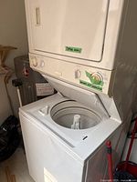 Full view of stacked washer and dryer, washer lid open, indicating dryer works and washer needs repair.