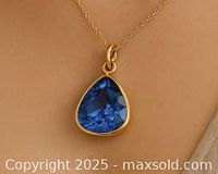 Pendant with triangular deep blue tanzanite gemstone in 10k gold bezel on a fine gold chain, worn on a back background.