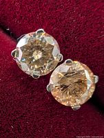 Close-up photo of two round-cut moissanite stones set in 14k white gold four-prong stud earring settings on red velvet background.