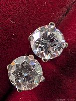 Two round diamond stud earrings in 4-prong white gold setting on burgundy background