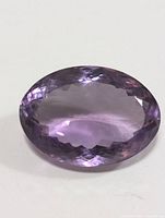 Close-up photo of large faceted oval cut amethyst gemstone showing purple color and facets clearly.