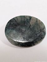 Oval cut 34 carat emerald loose gemstone showing dark and light green colors with internal inclusions, front view.