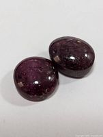 Two deep reddish-purple oval cabochon star ruby gemstones placed on white background, showing surface reflections and internal inclusions with asterism effect.
