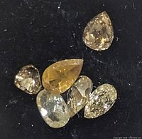 Six loose fancy color diamonds on black background showing different shapes and color tones from yellow to brown.