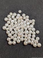 Loose genuine fresh water pearls scattered on a dark surface, showing a collection of various sizes and white color lustrous pearls