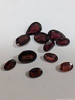 Nine faceted garnet gemstones arranged together on a white background showing varying shapes and sizes.