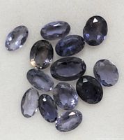 Lot of 15 oval-shaped faceted Iolite gemstones loosely placed on a white surface showing their color and cut details.