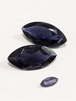Three marquise cut iolite gemstones on a white background showing color and clarity variations.