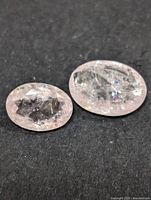 Two genuine morganite stones placed on a dark surface showing their oval shape, pale pink color, and internal inclusions.