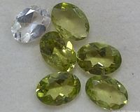 Six oval faceted gemstones including five green peridot and one clear stone.