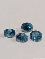 Four blue zircon faceted gemstones laid out on white background showing top and side facets.