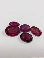 Five loose genuine ruby gemstones laid on white surface, showing their shapes, color, and faceting.