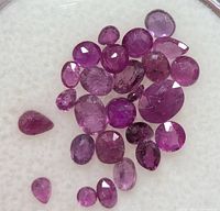 Close-up of multiple small faceted ruby stones with varying shapes and depths of color on white background.