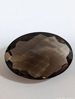 Oval faceted smokey quartz gemstone showing multiple facets and translucent brownish color.