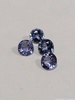 Four round-cut tanzanite stones arranged loosely on a neutral surface showing their violet-blue color and faceting.