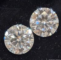 Close-up photo showing two round-cut clear gemstones with high brilliance and light reflection placed on a black background.