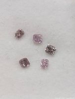 Close-up photo of five small natural pink color diamonds on white background showing details and color variation.
