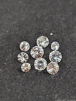 Close-up photo of nine round cut white sapphire loose stones on black background showing clarity and faceting.