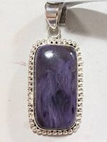 Front view of rectangular purple charolite stone pendant set in silver with beaded border and polished silver bail.
