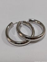 Pair of silver hoop earrings shown side by side on a white surface.