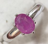 Close-up front view of an oval faceted natural ruby ring set in sterling silver band, showing smooth polished silver and natural ruby inclusions.