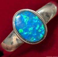 Close-up image showing the iridescent blue and green opalite stone set in a silver band with visible surface wear.