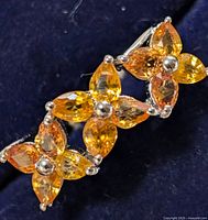 Close-up view of three orange sapphire flower clusters arranged on silver ring band.