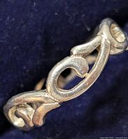 Close-up photo of a silver ring showing a scroll leaf design on the band.